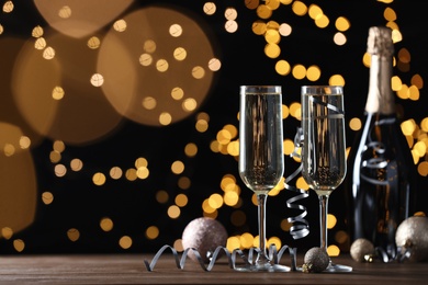 Photo of Glasses and bottle of champagne, Christmas decor with serpentine streamers against blurred lights. Space for text