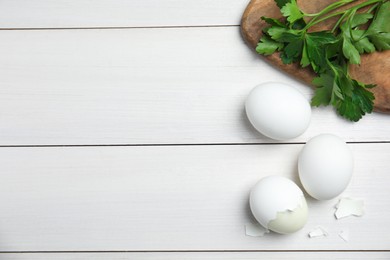 Photo of Boiled eggs, pieces of shell and parsley on white wooden table, flat lay