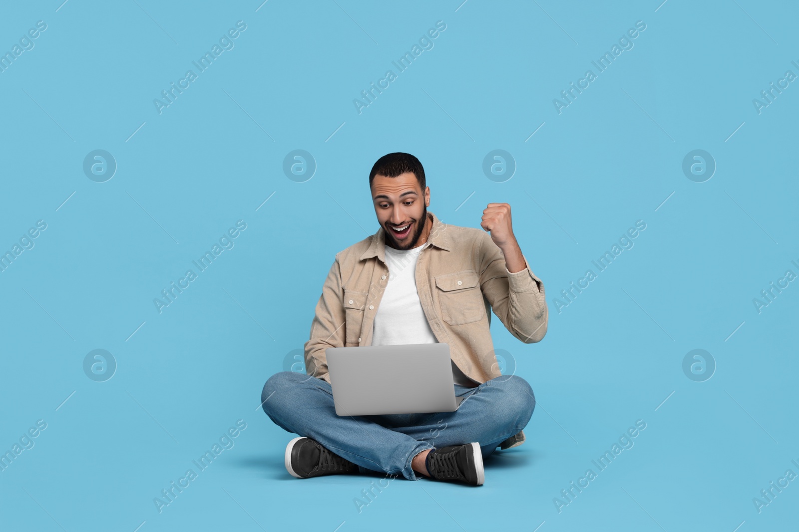 Photo of Happy young man with laptop on light blue background