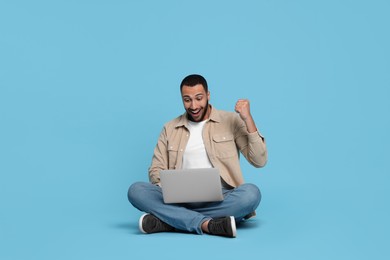 Happy young man with laptop on light blue background