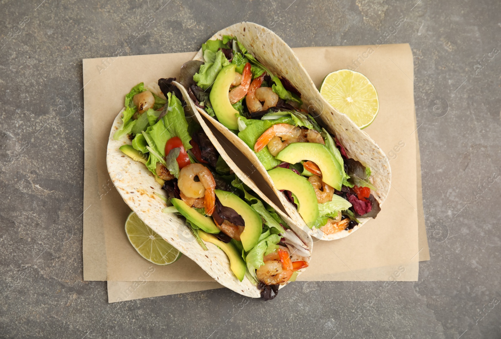Photo of Delicious tacos with shrimps, avocado and lime on grey table, top view