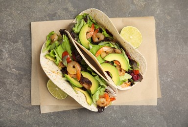 Delicious tacos with shrimps, avocado and lime on grey table, top view