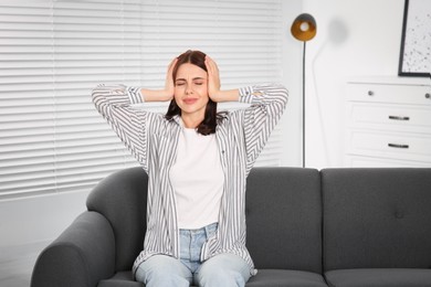 Photo of Young woman suffering from headache on sofa at home. Hormonal disorders