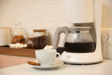 Photo of Modern coffeemaker and cup with cookie on table in kitchen