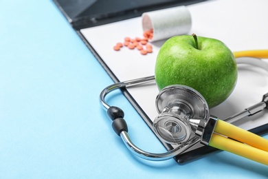 Composition with stethoscope, clipboard, pills and apple on color background. Medical equipment