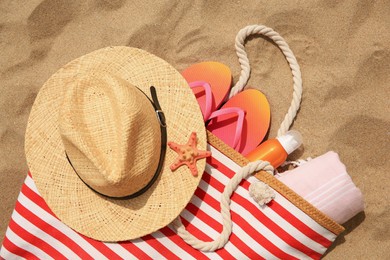 Photo of Stylish striped bag with beach accessories on sand, flat lay