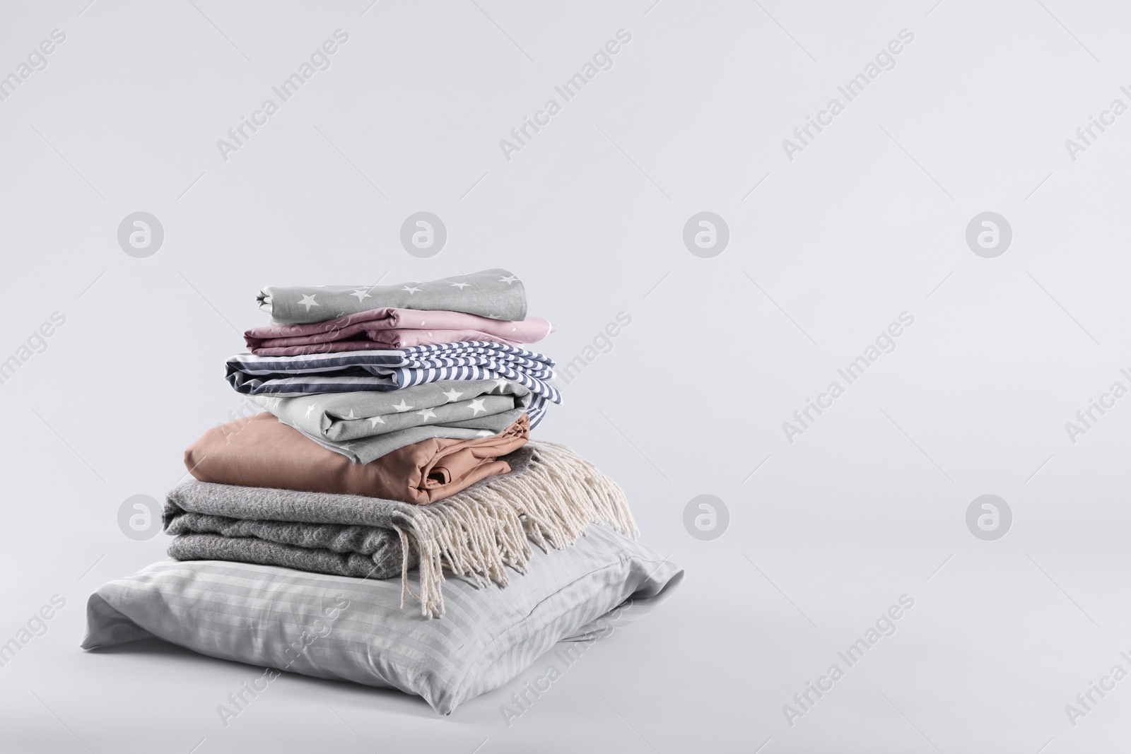 Photo of Stack of clean bed sheets and pillow on white background. Space for text