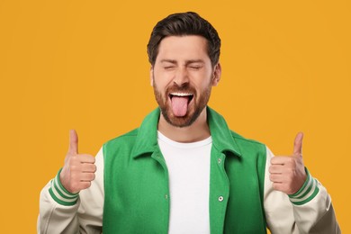 Man showing his tongue and thumbs up on orange background