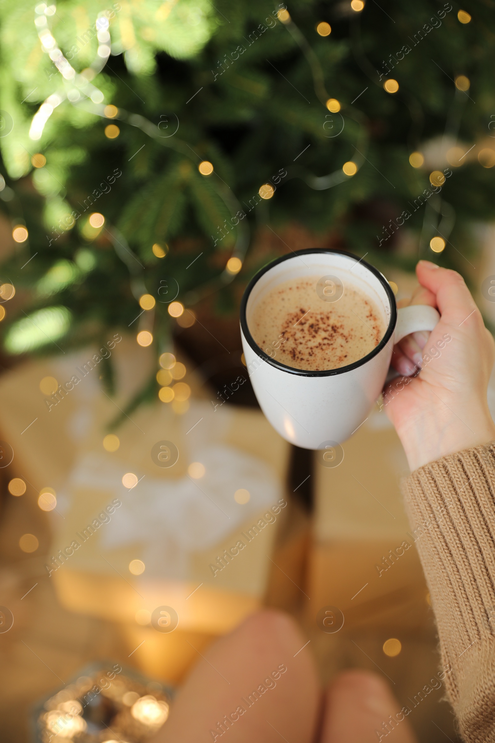 Photo of Woman holding cup of cocoa near Christmas tree indoors, closeup