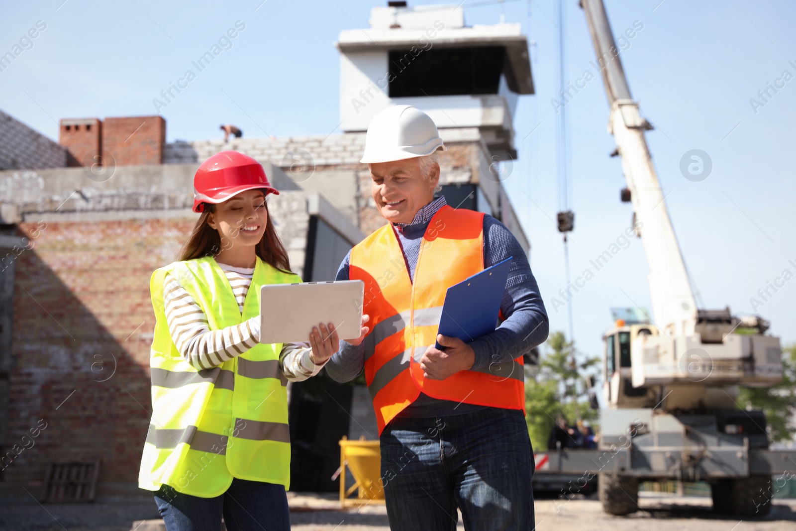 Photo of Professional engineer and foreman in safety equipment with tablet at construction site