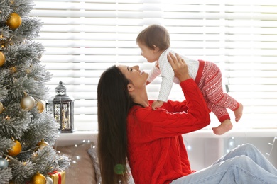 Photo of Mother and her cute baby near Christmas tree at home