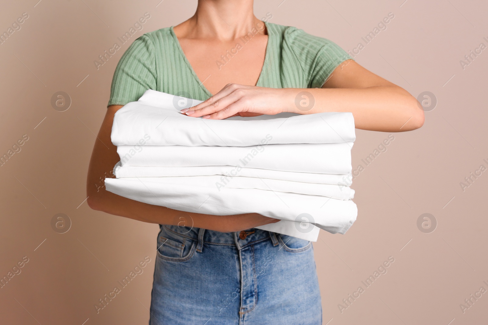 Photo of Woman holding stack of clean bed linens on beige background