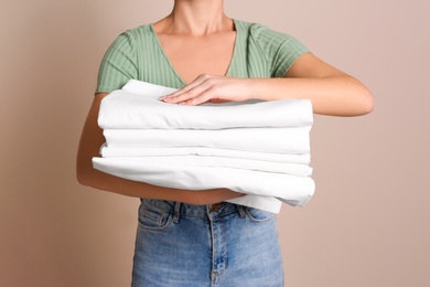 Woman holding stack of clean bed linens on beige background