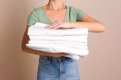 Photo of Woman holding stack of clean bed linens on beige background