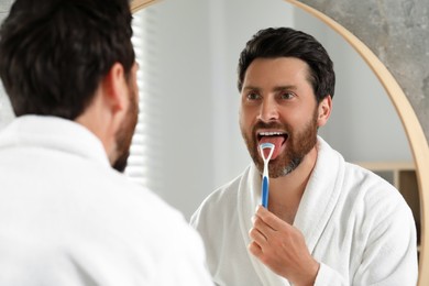 Photo of Handsome man brushing his tongue with cleaner near mirror in bathroom