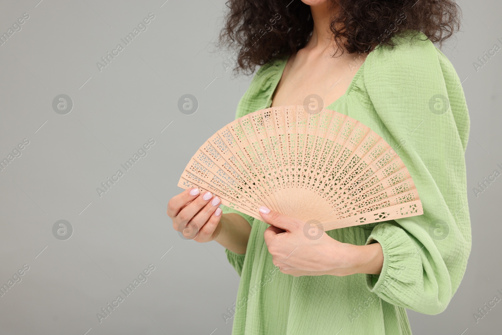 Photo of Woman holding hand fan on light grey background, closeup. Space for text