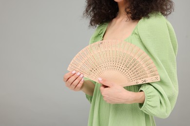 Photo of Woman holding hand fan on light grey background, closeup. Space for text