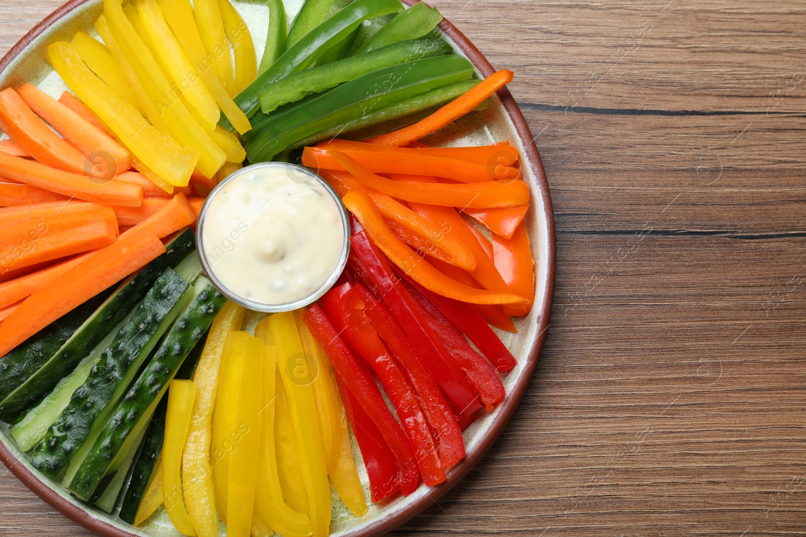 Photo of Fresh raw vegetable sticks and sauce on wooden table, top view