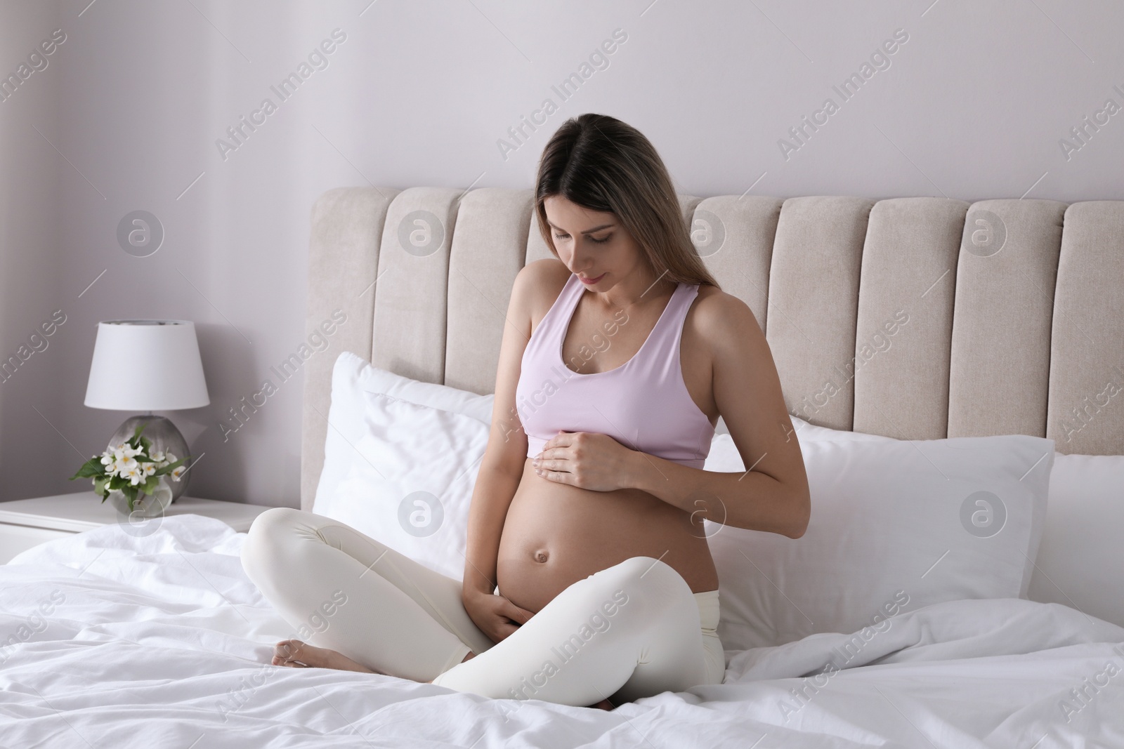 Photo of Beautiful pregnant woman sitting on bed at home