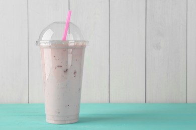 Tasty smoothie in plastic cup on light blue table against white wooden wall. Space for text