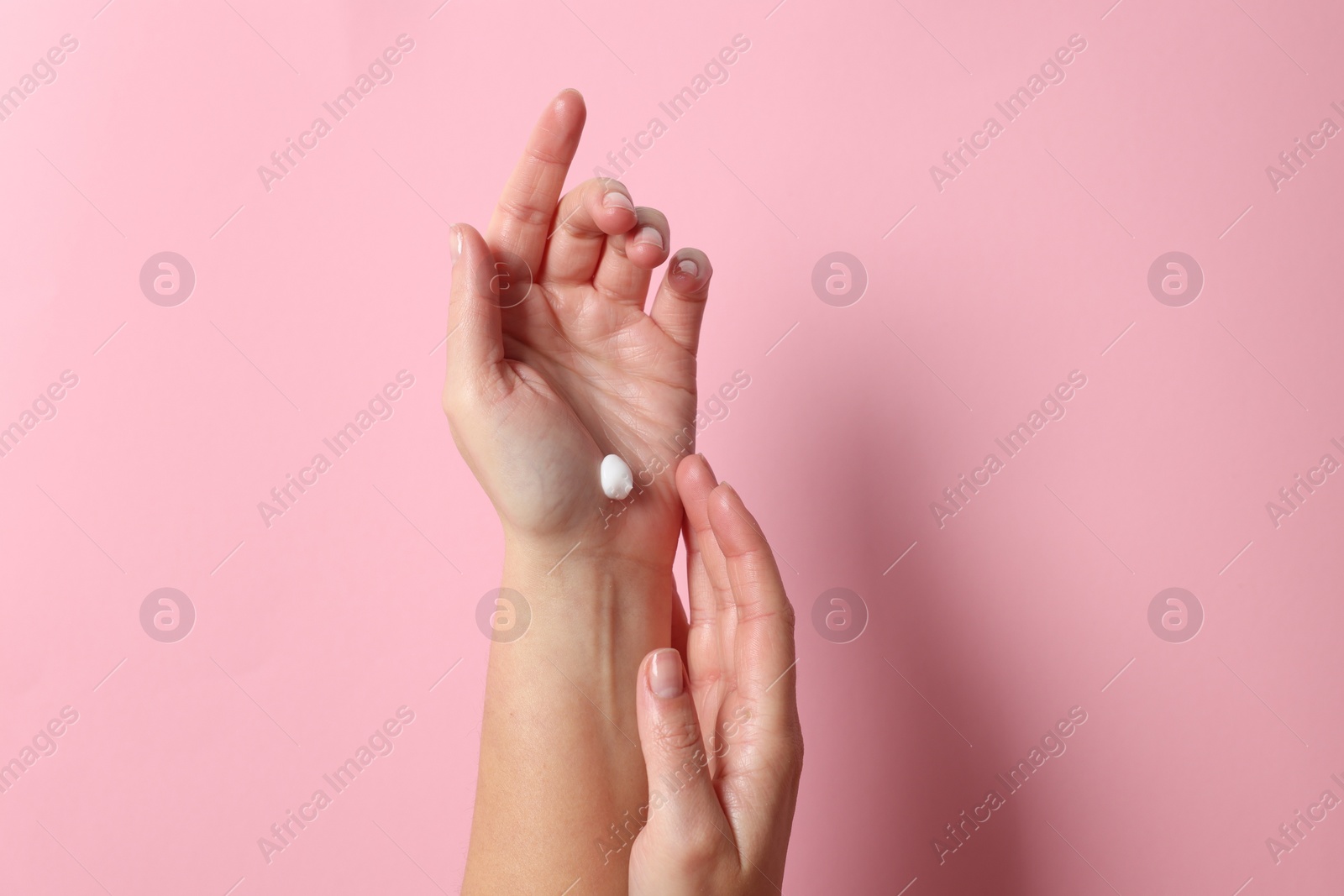 Photo of Woman applying cosmetic cream onto hand on pink background, top view