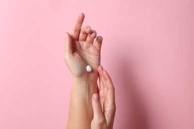 Photo of Woman applying cosmetic cream onto hand on pink background, top view