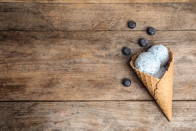 Delicious ice cream in waffle cone and blueberries on wooden table, space for text