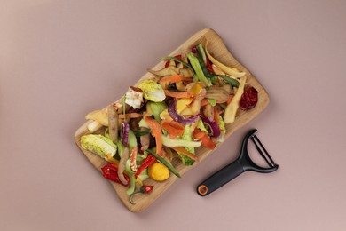 Photo of Peels of fresh vegetables and peeler on dusty pink background, flat lay