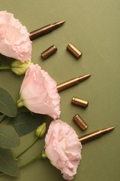 Photo of Bullets, cartridge cases and beautiful eustoma flowers on green background, flat lay