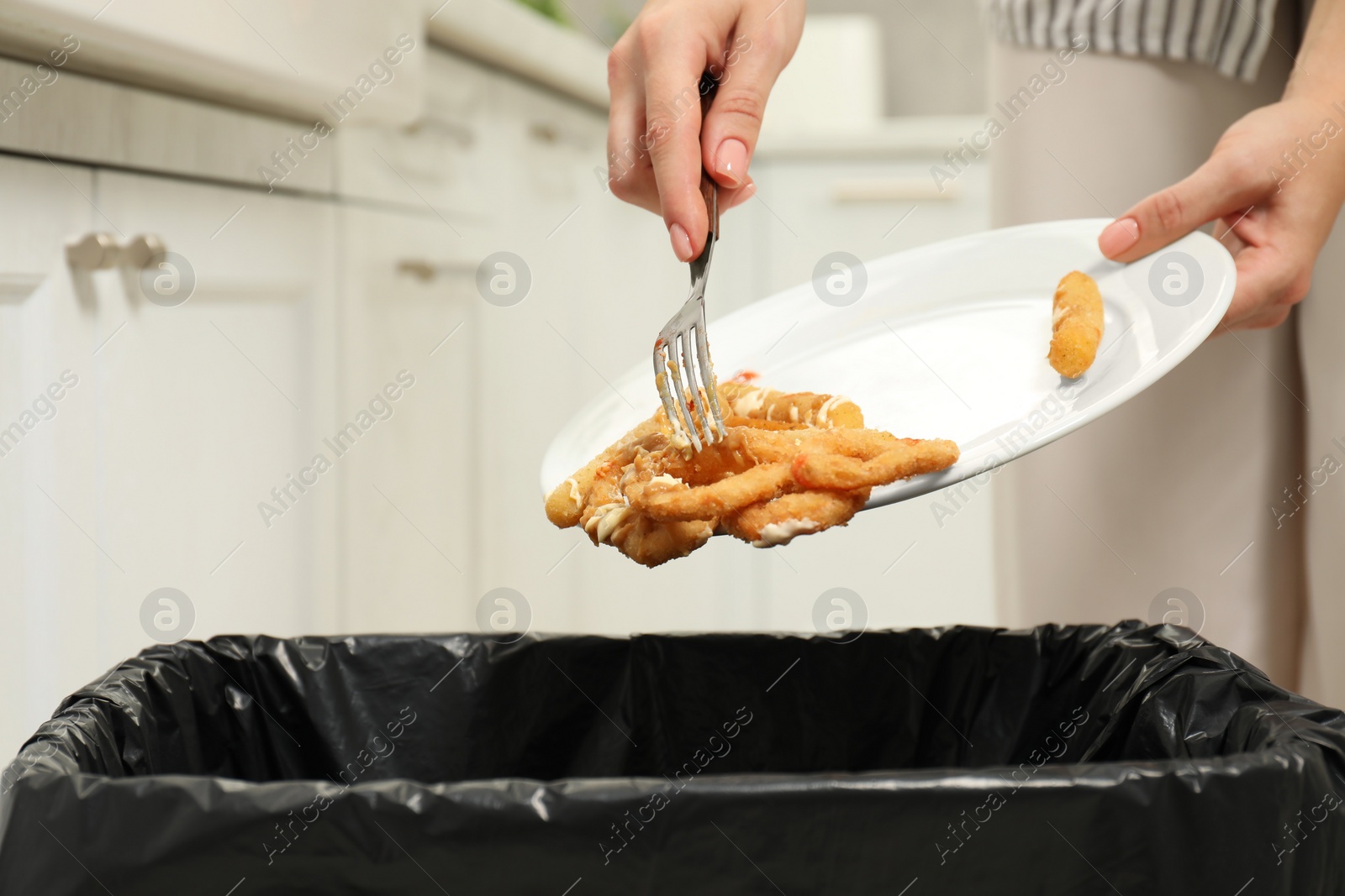 Photo of Woman throwing onion rings into bin indoors, closeup