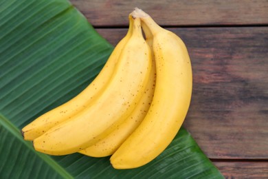 Photo of Delicious bananas and green leaf on wooden table, top view