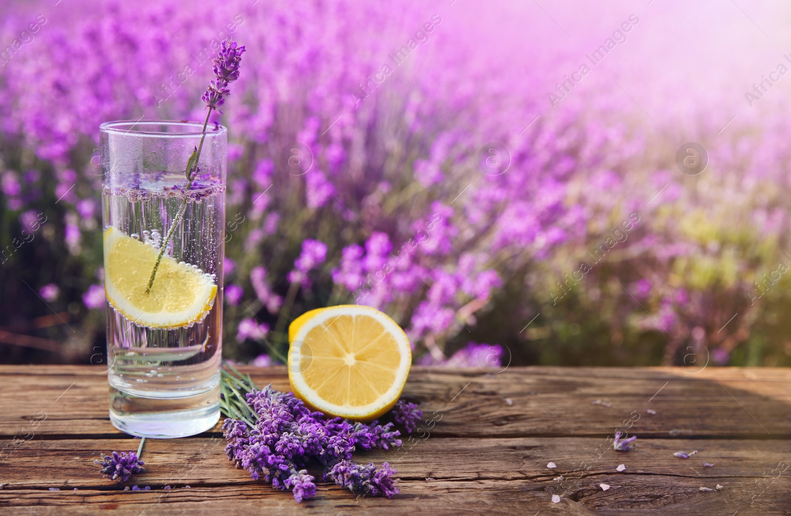 Photo of Lemonade with lemon slice and lavender flowers on wooden table outdoors. Space for text