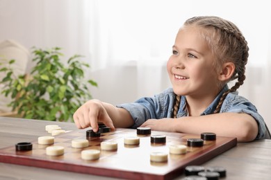 Photo of Playing checkers. Little girl thinking about next move at table in room