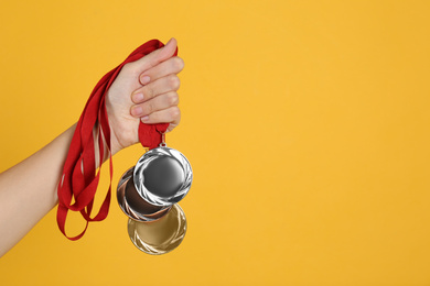 Photo of Woman holding medals on yellow background, closeup. Space for design