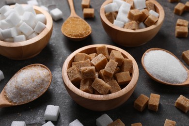 Photo of Bowls and spoons with different types of sugar on gray table