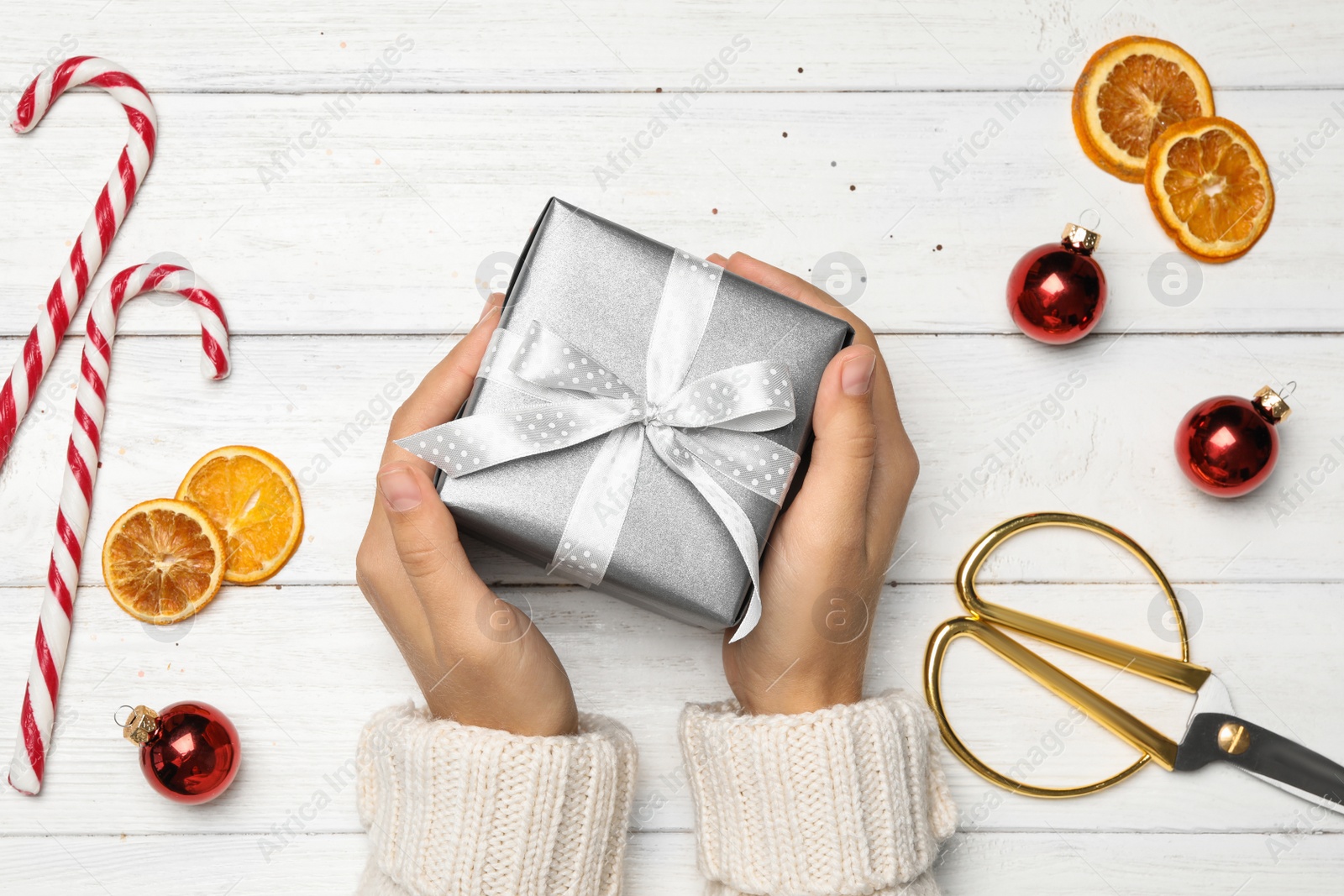 Photo of Young woman holding Christmas gift on white wooden background, flat lay