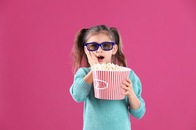 Cute little girl with popcorn and glasses on color background