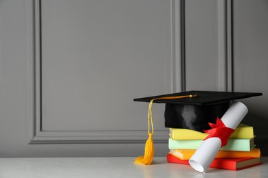 Photo of Graduation hat, books and diploma on white table near grey wall, space for text