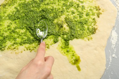 Making delicious pesto bread. Woman putting sauce onto raw dough at grey table, top view