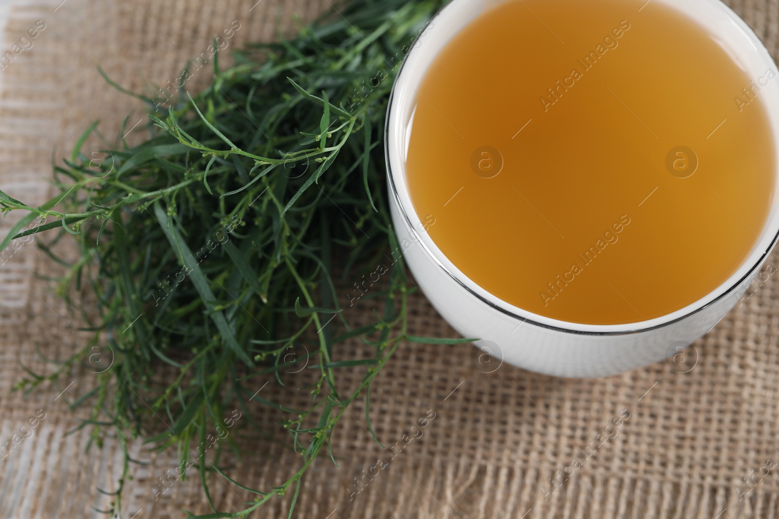 Photo of Aromatic herbal tea and fresh tarragon sprigs on table, above view