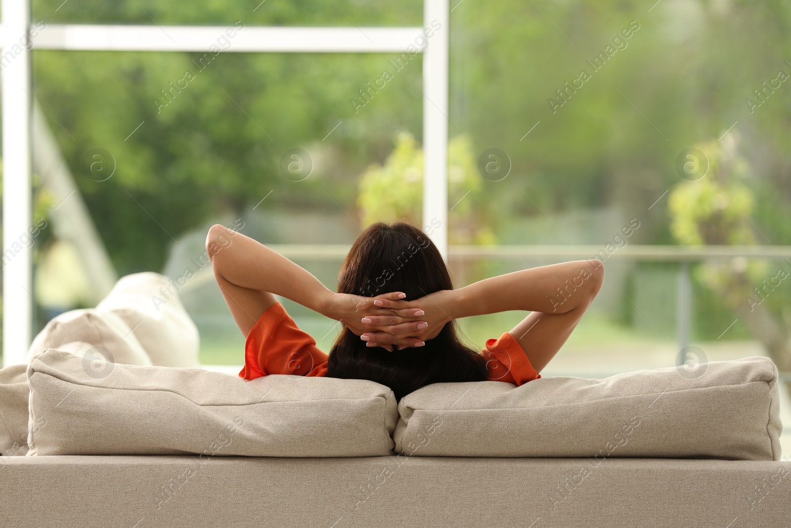 Photo of Young woman relaxing on sofa at home, back view