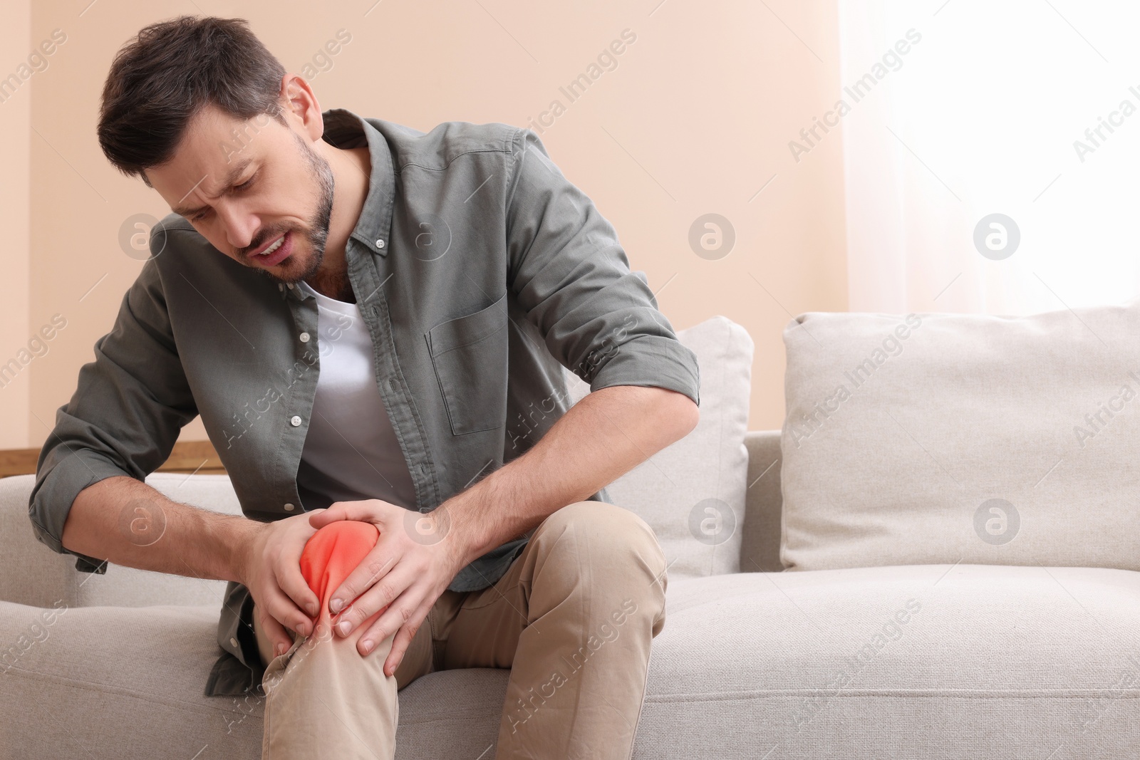 Image of Man suffering from pain in knee on sofa at home. Space for text