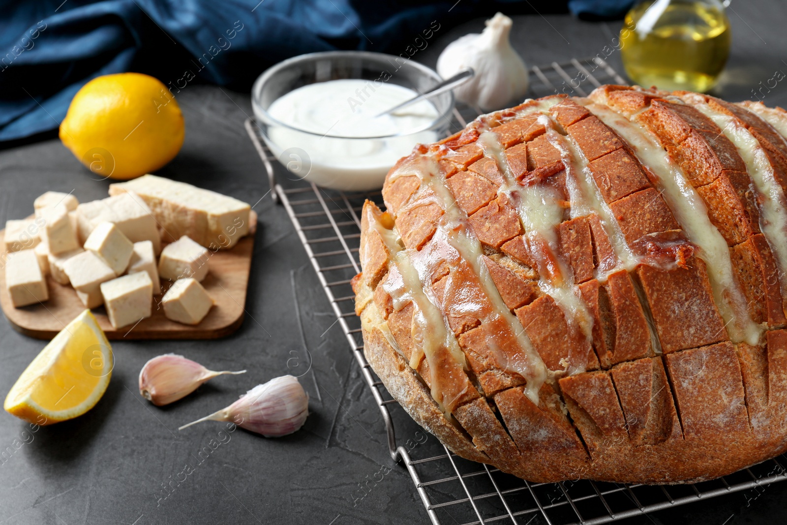 Photo of Freshly baked bread with tofu cheese and ingredients on black table, closeup