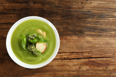 Delicious asparagus soup in bowl on wooden table, top view. Space for text