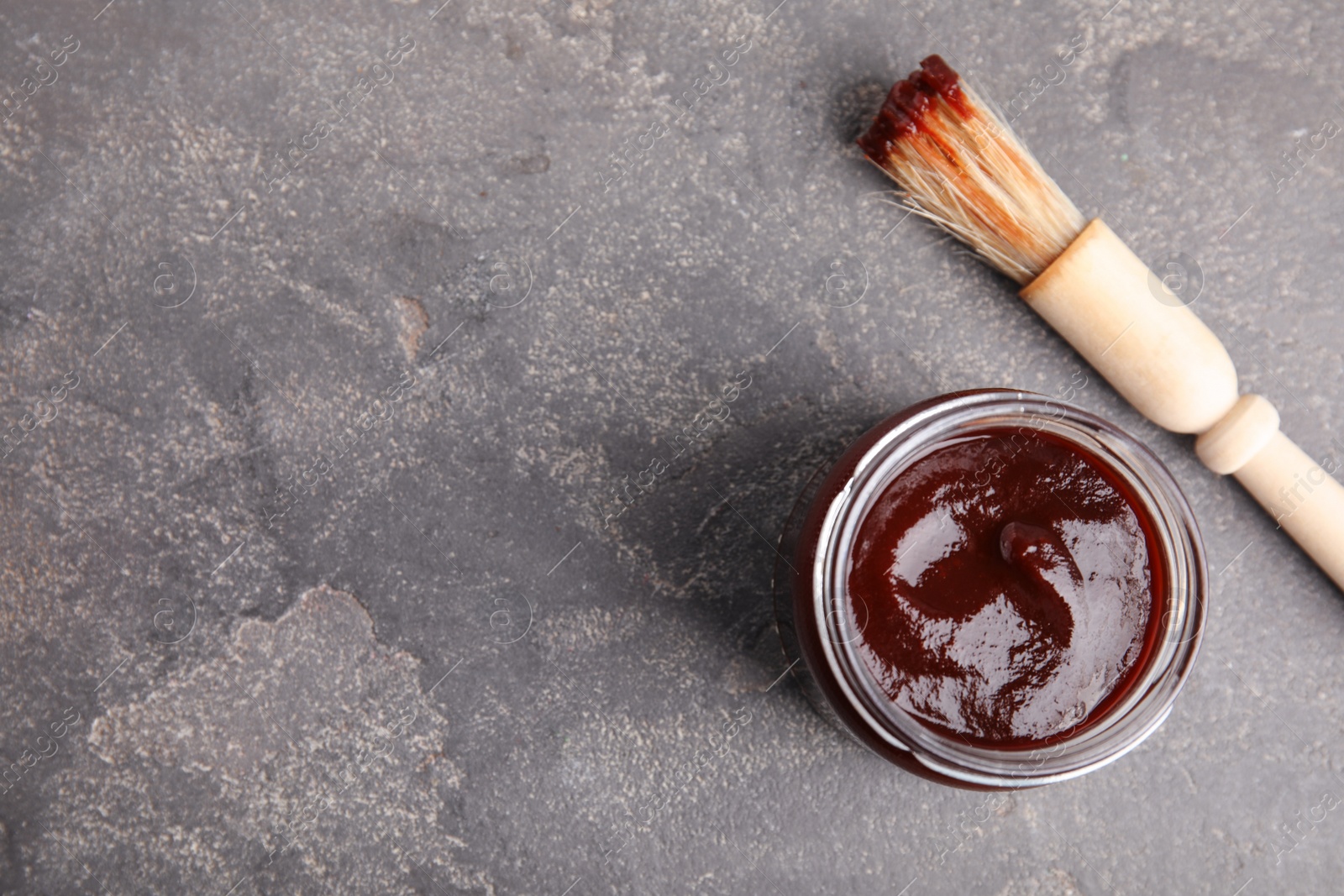 Photo of Jar with barbecue sauce and brush on grey background, flat lay. Space for text