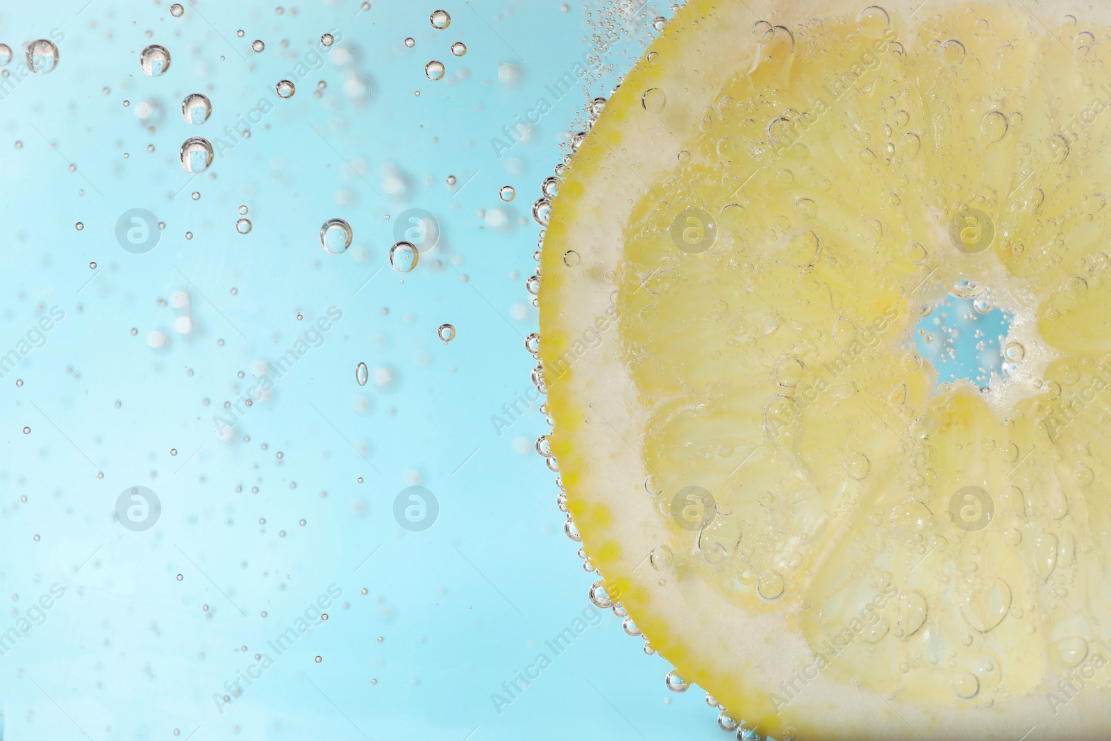 Photo of Juicy lemon slice in soda water against light blue background, closeup. Space for text