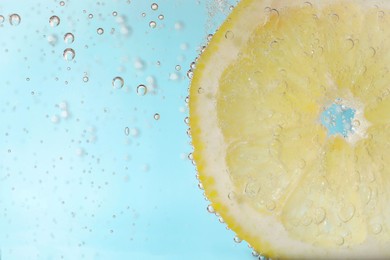 Photo of Juicy lemon slice in soda water against light blue background, closeup. Space for text