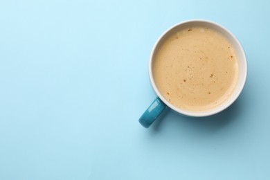 Fresh coffee in cup on light blue background, top view. Space for text