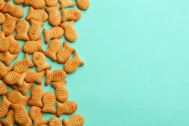 Photo of Delicious goldfish crackers on turquoise background, flat lay. Space for text