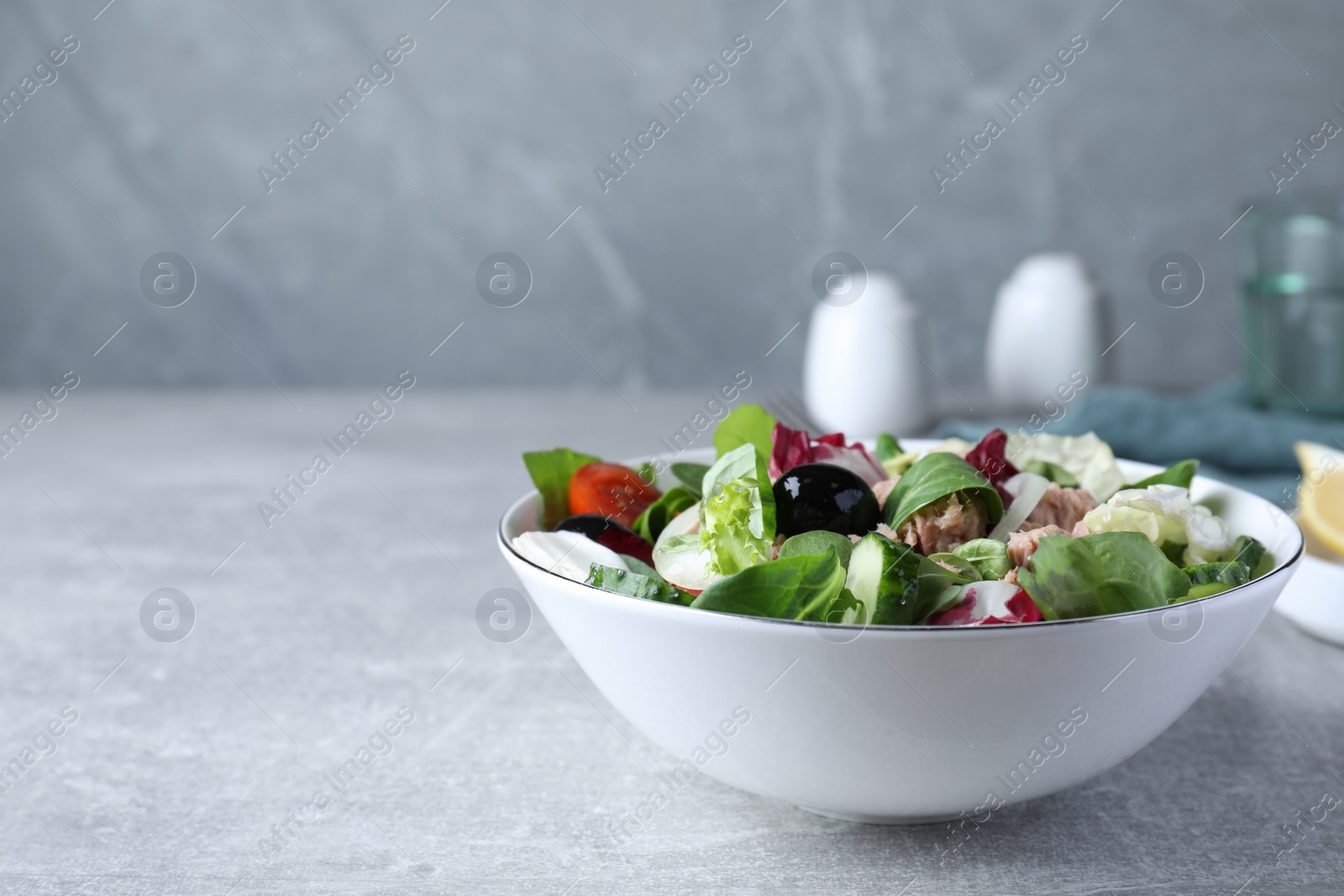 Photo of Bowl of delicious salad with canned tuna and vegetables on light grey table, space for text